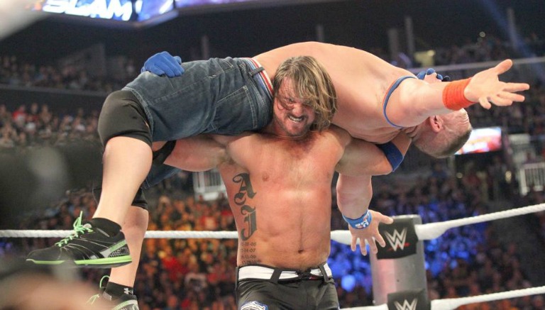 AJ Styles carga a John Cena durante el combate