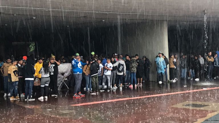 Aficionados de Pumas se cubren de la lluvia bajo un puente